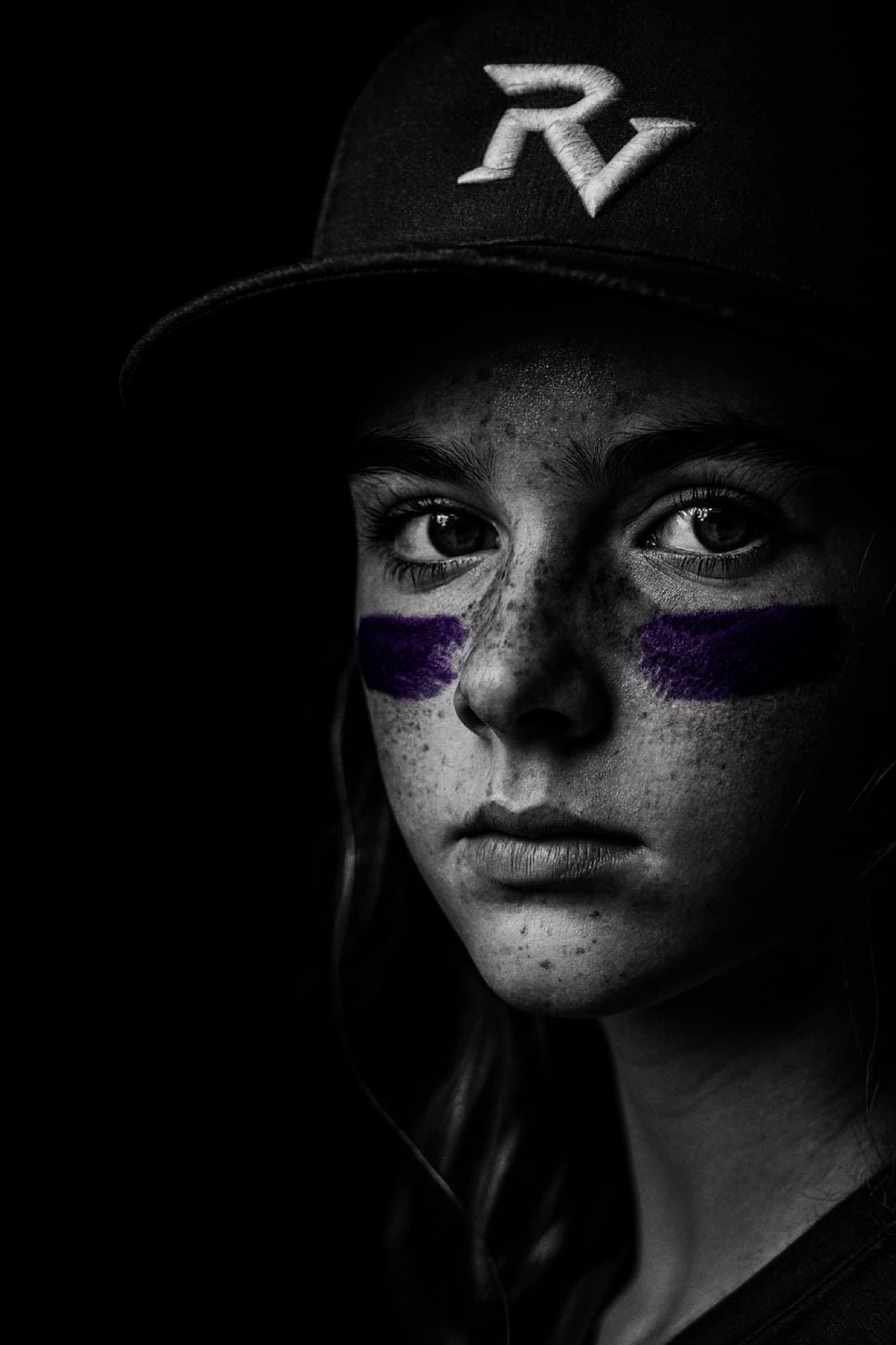 Half of a Ravens softball player's face at the edge of the frame, purple eye black under her eye
